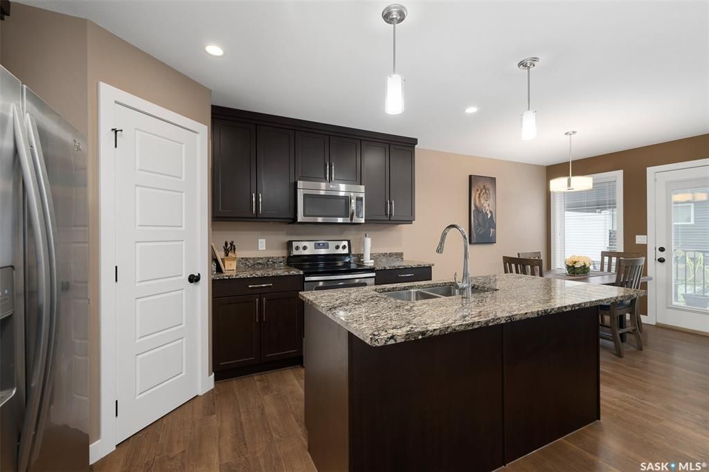 Kitchen with sink, a kitchen island with sink, appliances with stainless steel finishes, pendant lighting, and dark wood-type flooring
