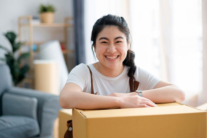 A woman leans over a packing box with a big smile on her face.